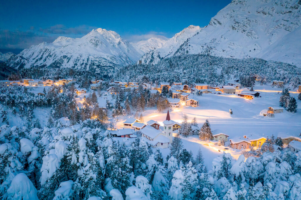 Un pueblo suizo paradisíaco con suaves luces amarillas, rodeado de montañas alpinas y cubierto de nieve.