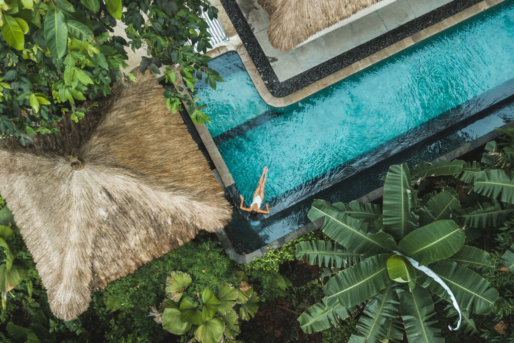 Vista aérea de una mujer descansando en una piscina en medio de follaje tropical.