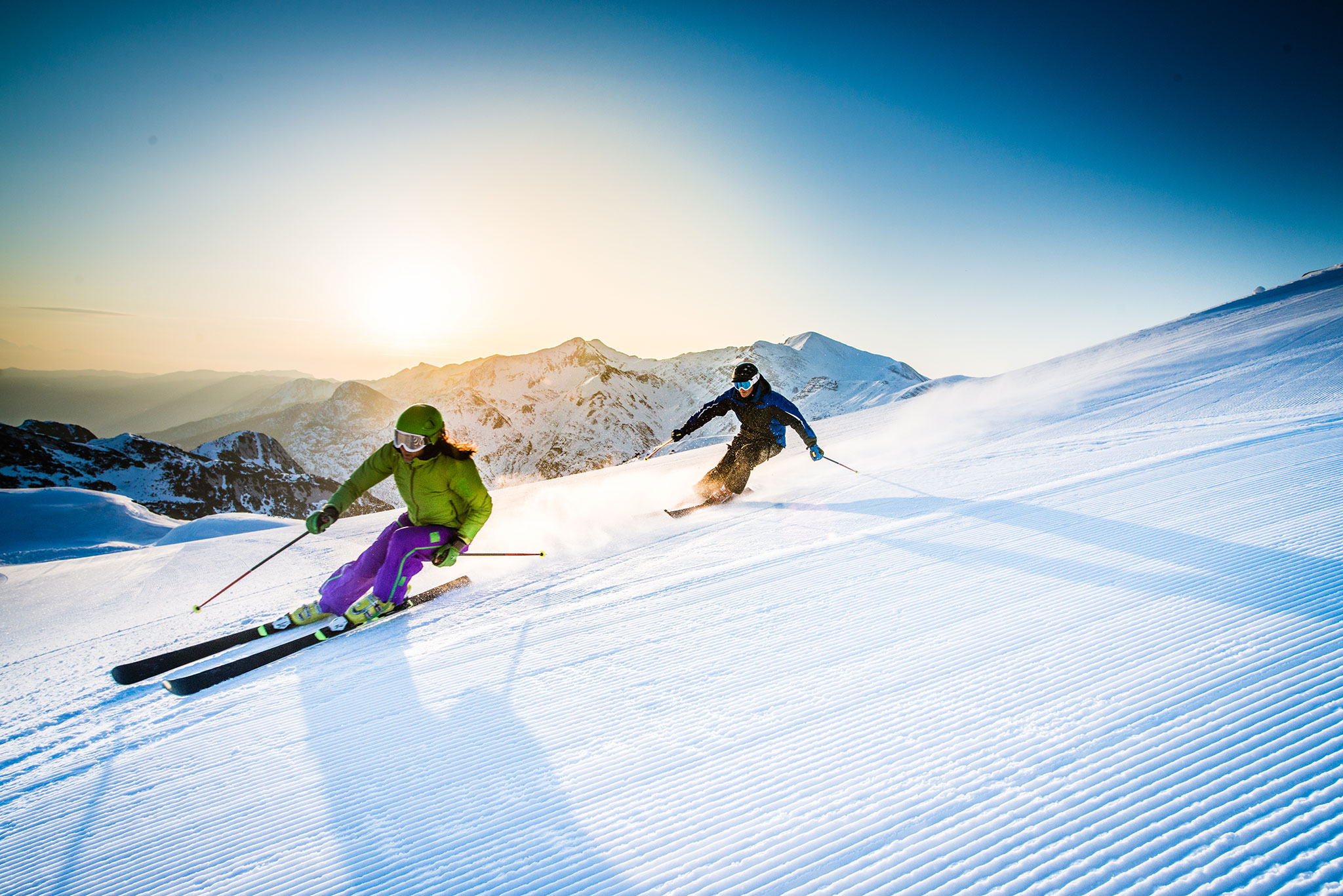 Dos esquiadores en nieve se inclinan en una curva sobre polvo fresco.