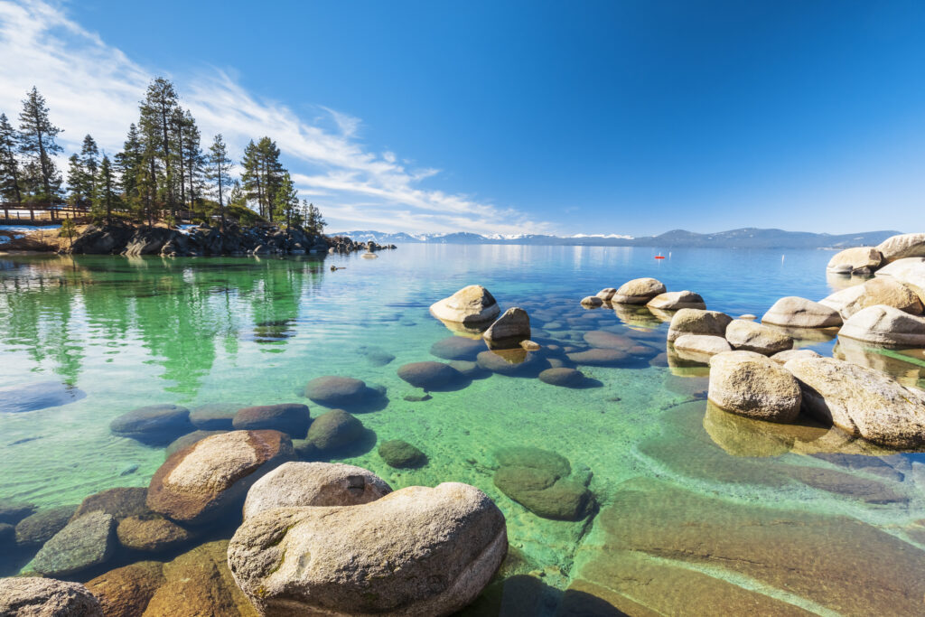Costa rocosa del lago Tahoe en un día soleado, playa con cielo azul sobre agua clara y transparente