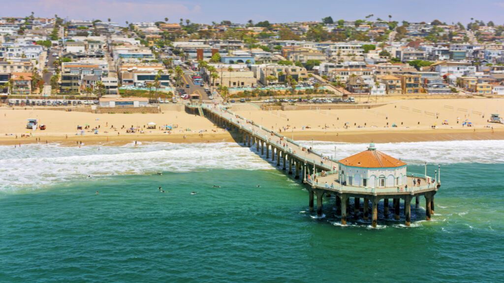Vista aérea del muelle de la playa de Huntington y de las olas que salpican la playa contra un barrio residencial, condado de Orange, sur de California, California, EE. UU.